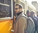 A stylish man with a backpack boards a tram in bustling Budapest, Hungary, during the day.